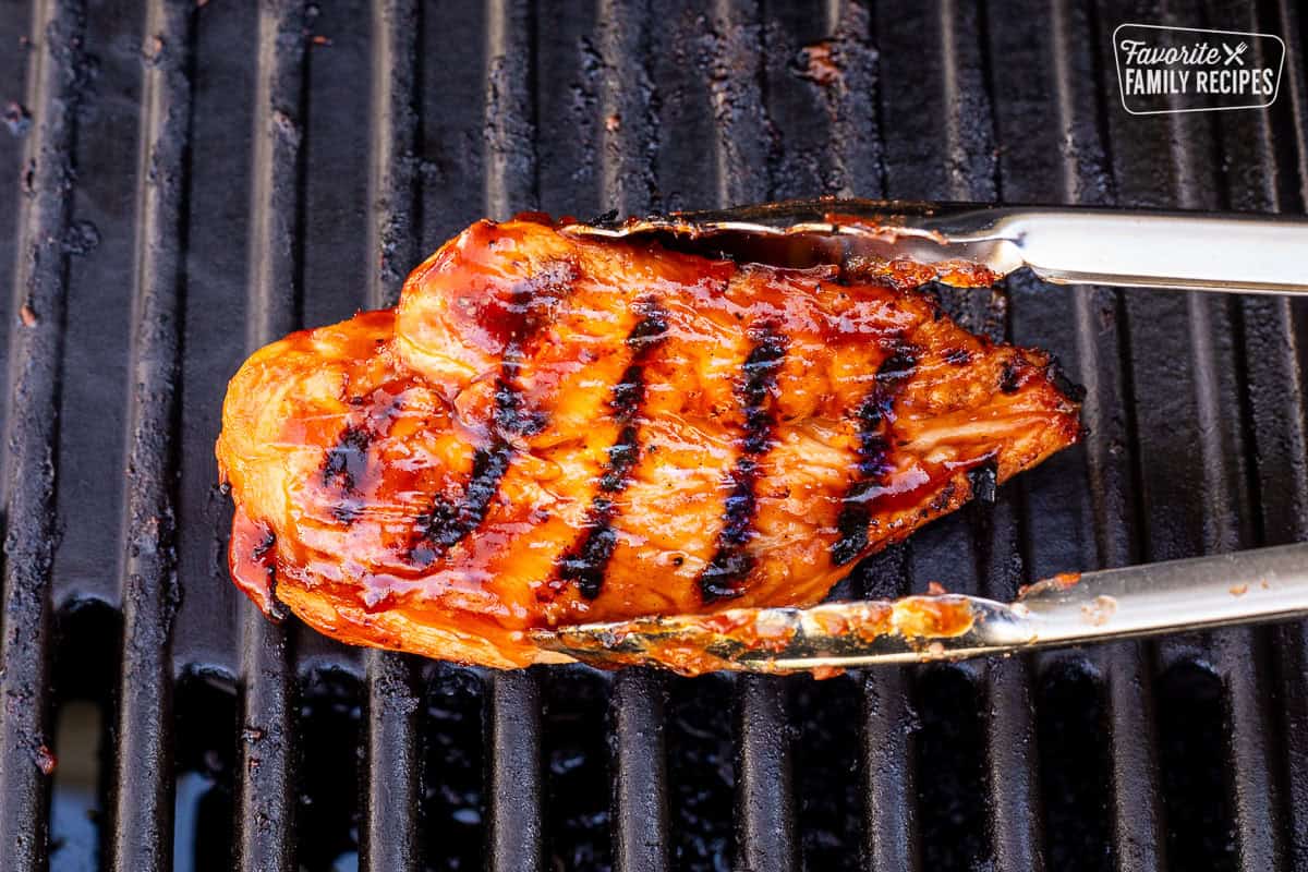 Removing barbecue chicken breast from the grill with tongs.