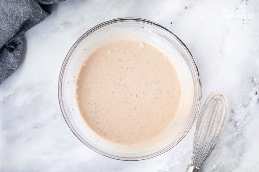 Glass bowl with combined barbecue sauce dressing and whisk on the side.