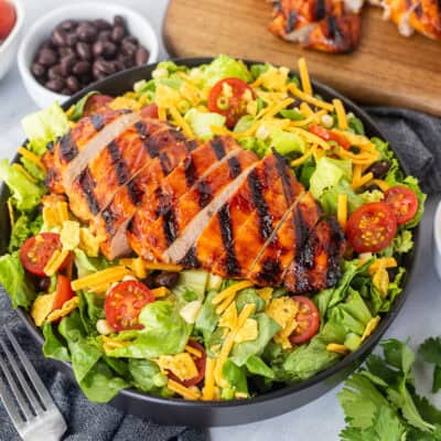 BBQ chicken salad with barbecue grilled chicken breast, lettuce, black beans, corn, tomatoes, crushed tortilla chips, green onion and shredded cheddar cheese. Creamy barbecue dressing on the side.