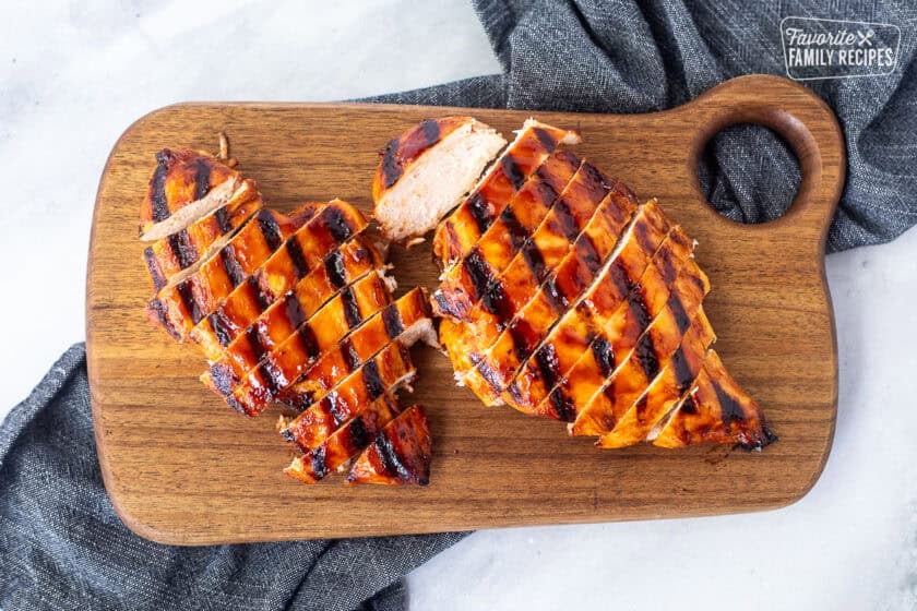 Two barbecue grilled chicken breasts sliced on a cutting board.