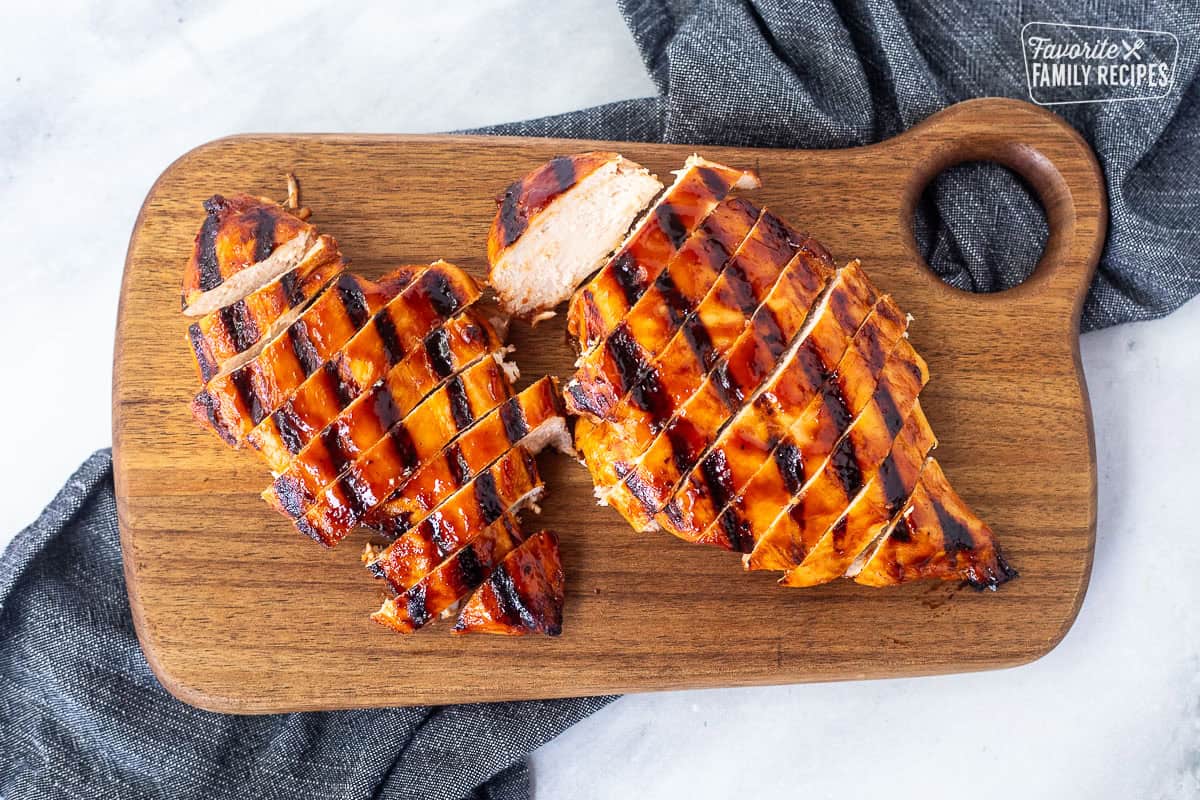 Two barbecue grilled chicken breasts sliced on a cutting board.