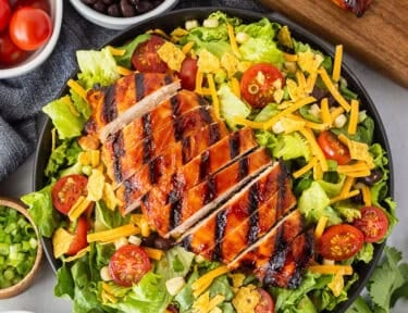 BBQ chicken salad with barbecue grilled chicken breast, lettuce, black beans, corn, tomatoes, crushed tortilla chips, green onion and shredded cheddar cheese. Creamy barbecue dressing on the side.