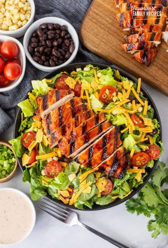 BBQ chicken salad with barbecue grilled chicken breast, lettuce, black beans, corn, tomatoes, crushed tortilla chips, green onion and shredded cheddar cheese. Creamy barbecue dressing on the side.