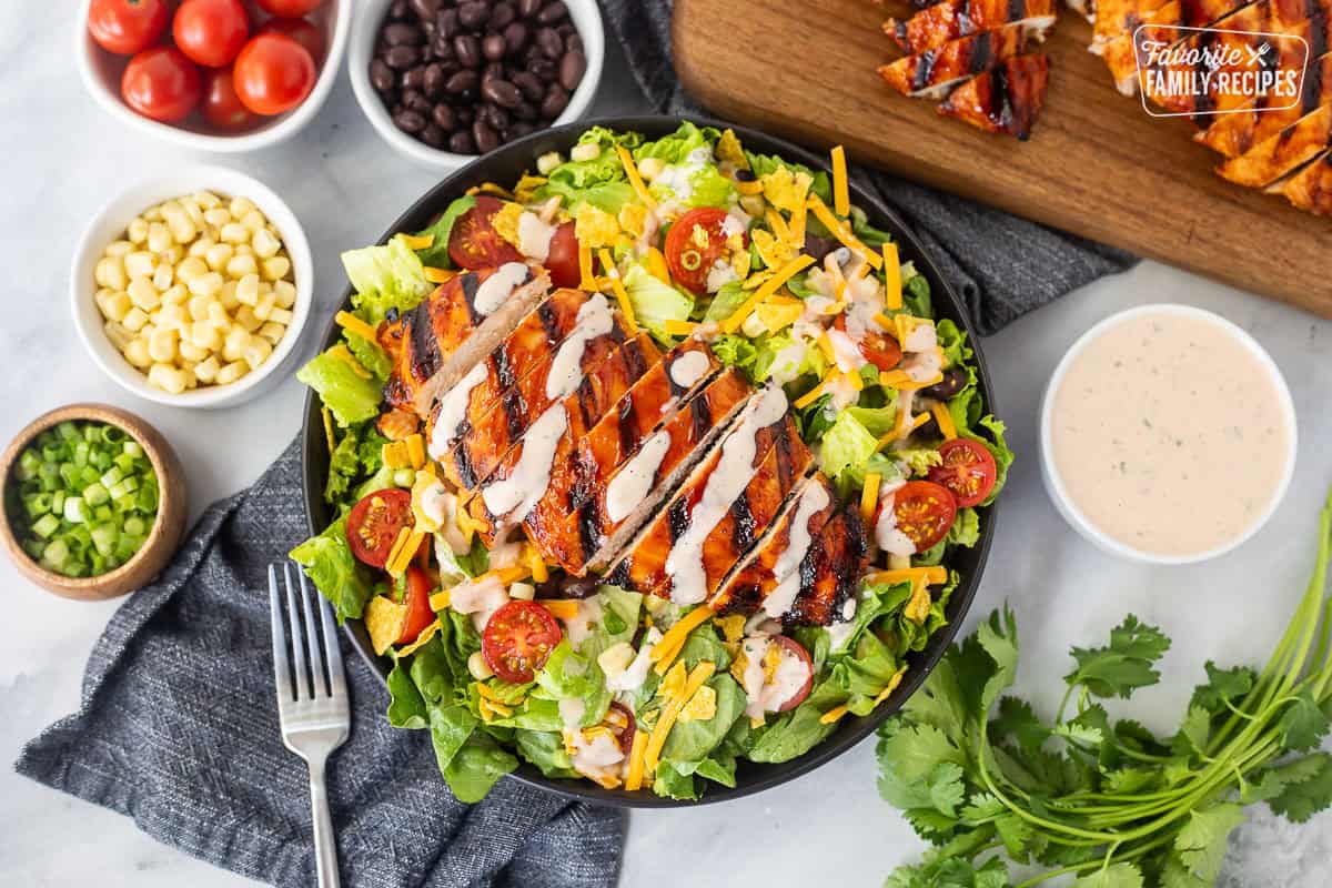 BBQ chicken salad with barbecue grilled chicken breast, lettuce, black beans, corn, tomatoes, crushed tortilla chips, green onion and shredded cheddar cheese. Drizzled with creamy barbecue dressing on top.
