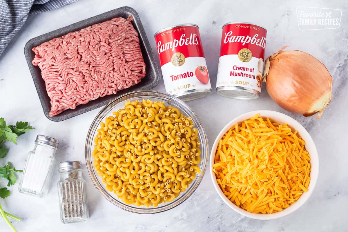 Ingredients to make Beefaroni including macaroni noodles, cheddar cheese, onion, cream of mushroom soup, tomato soup, ground beef, salt and pepper.