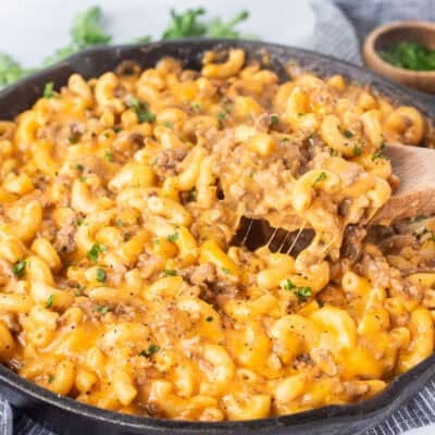 Scooping Beefaroni with a wooden spoon from a skillet.