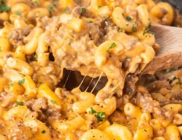 Scooping Beefaroni with a wooden spoon from a skillet.