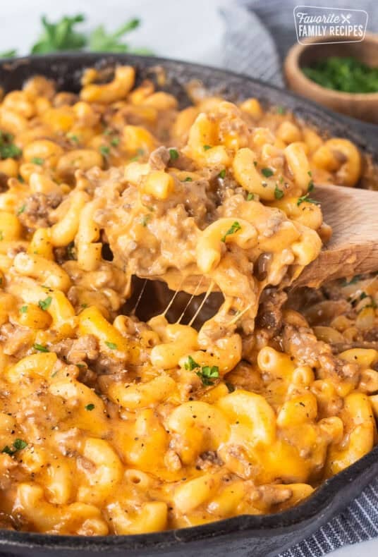 Scooping Beefaroni with a wooden spoon from a skillet.