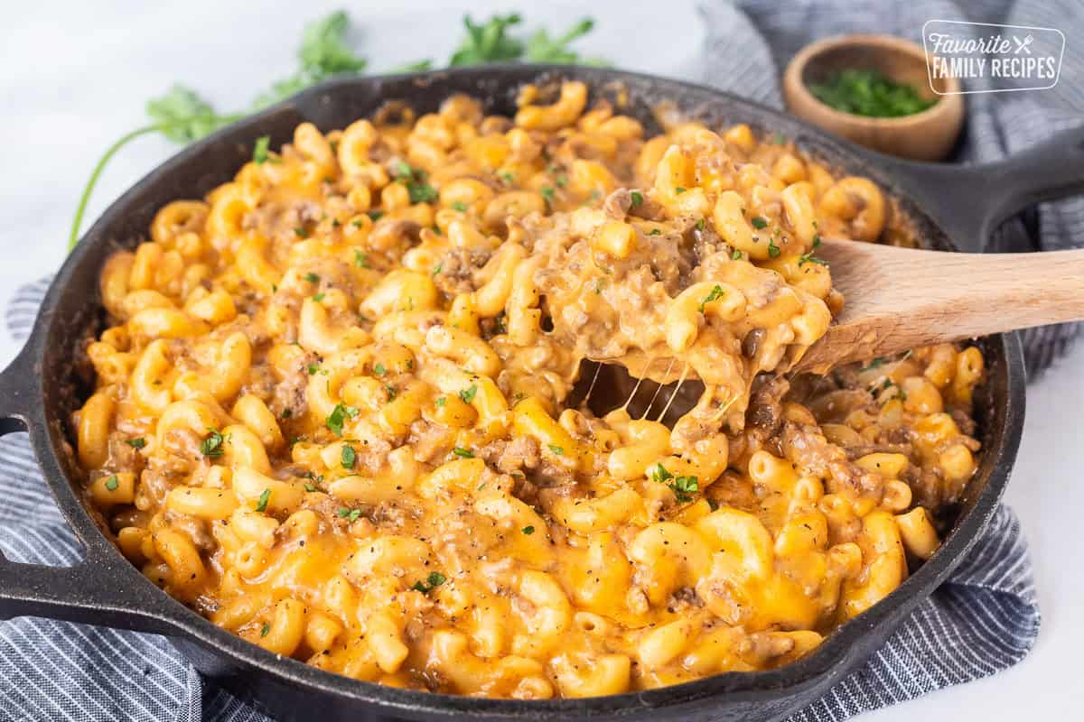 Scooping Beefaroni with a wooden spoon from a skillet.