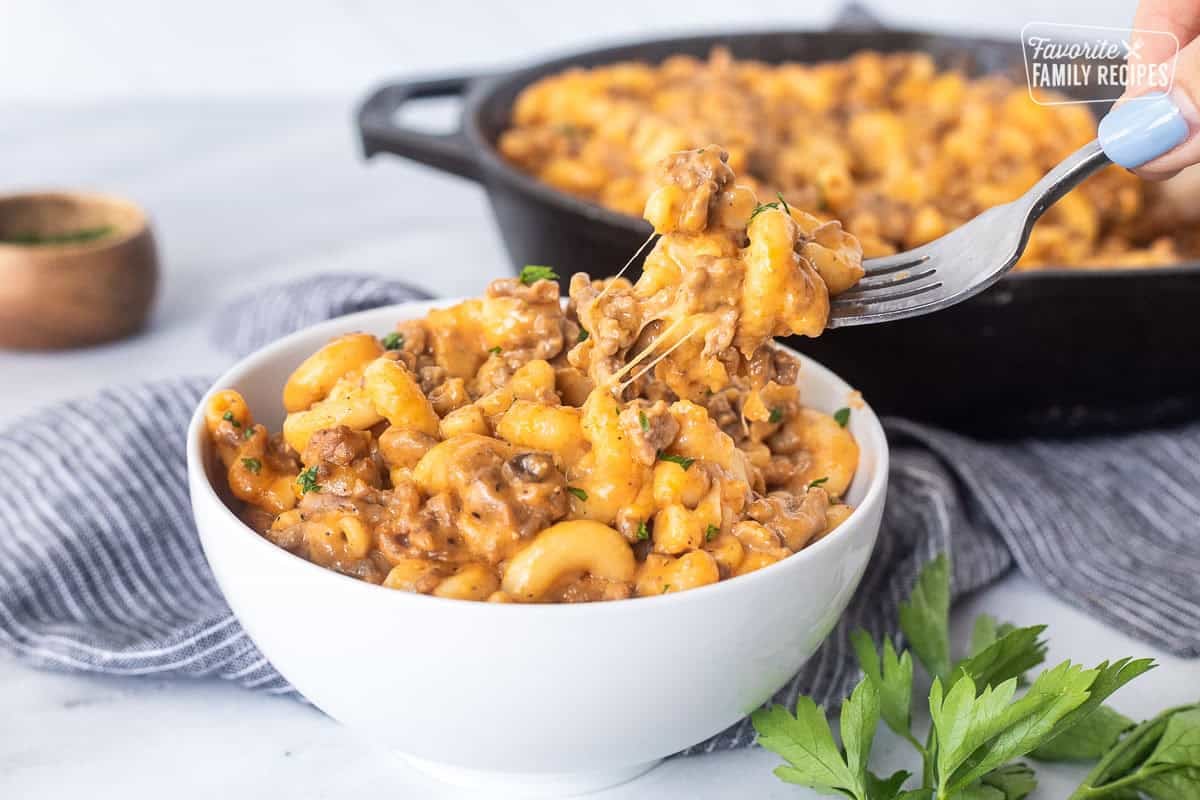 Cheesy noodles stretching from bowl of beefaroni with a fork.