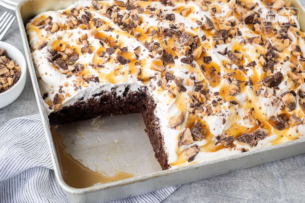 Slice missing from Better Than Sex Cake topped with crushed Heath bars and caramel sauce.