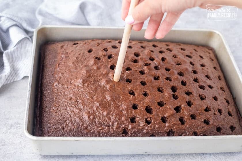 Poking holes into chocolate cake with a wooden spoon.