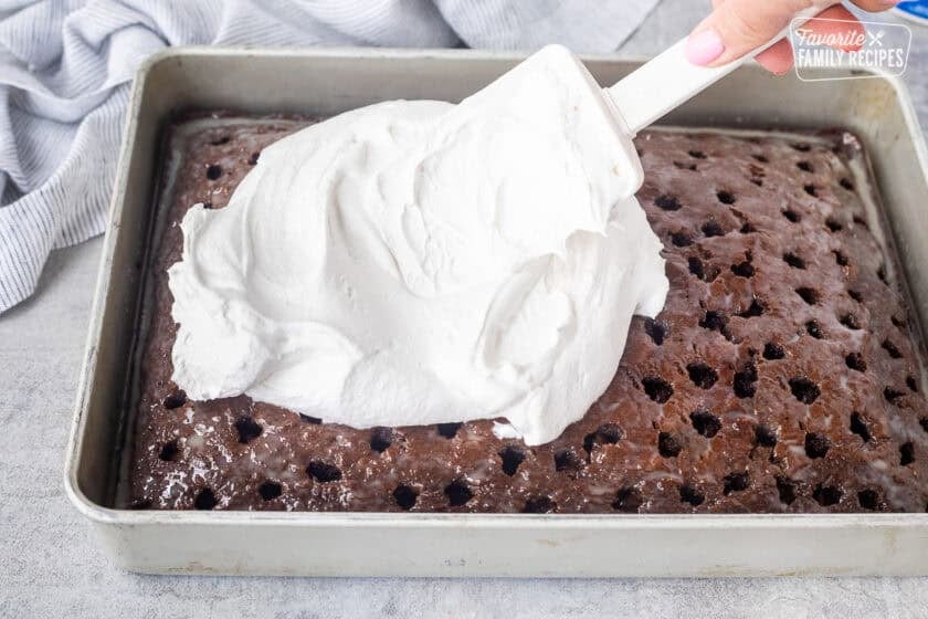 Spreading cool whip on top of of chocolate cake with holes and caramel sauce on top.