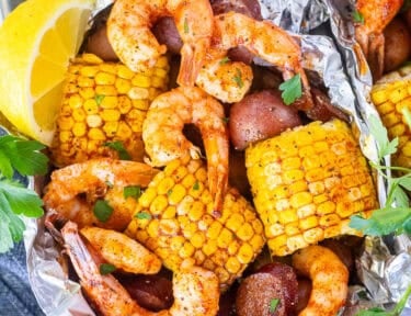 Cajun Foil Packet with shrimp, sausage, corn and red potatoes. Garnished with parsley and lemon wedges.