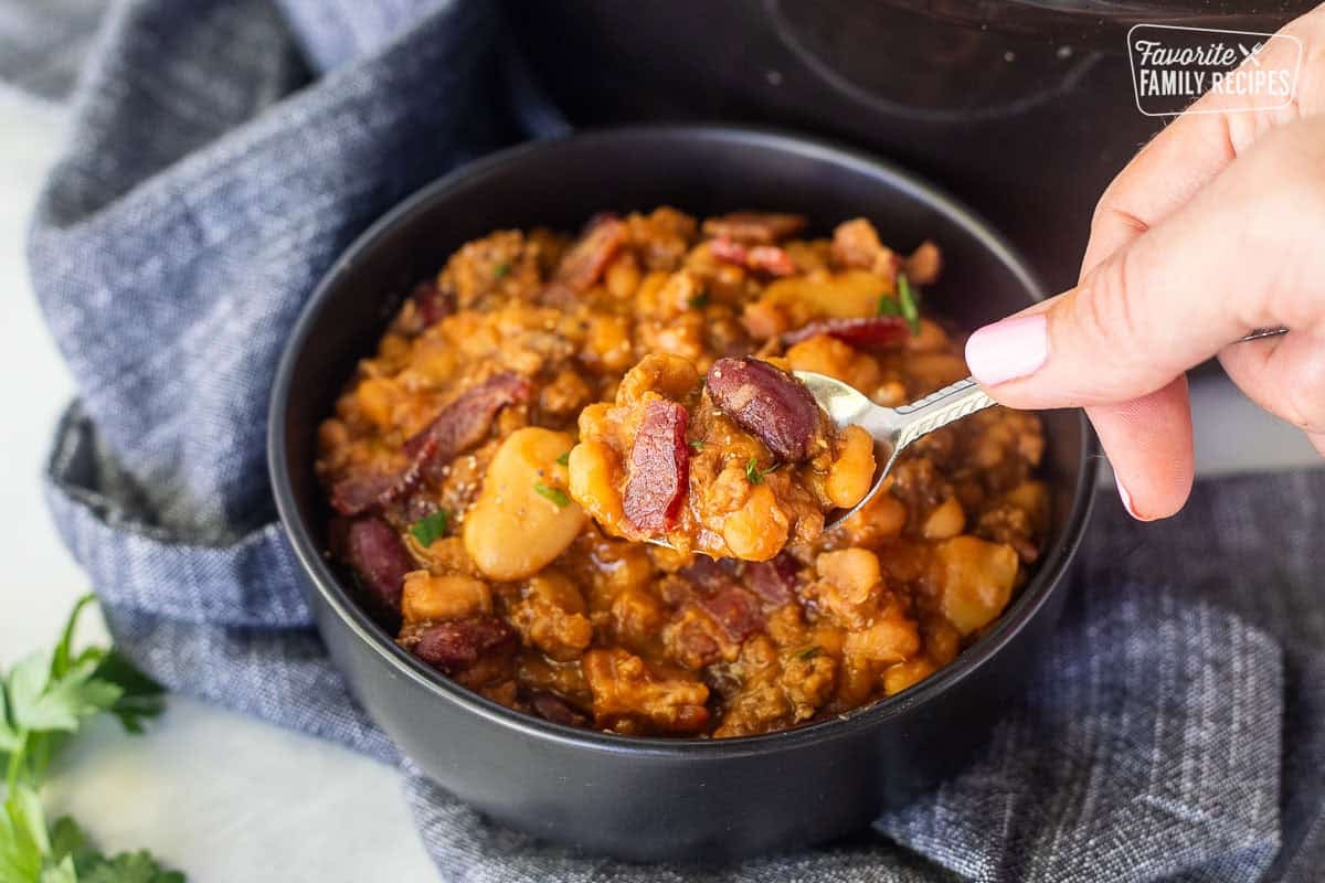 These Crockpot baked beans are the perfect side dish for your next potluck or BBQ. They are sweet, savory, beefy, hearty, and oh so delicious! Bowl of Calico beans with a spoon full.