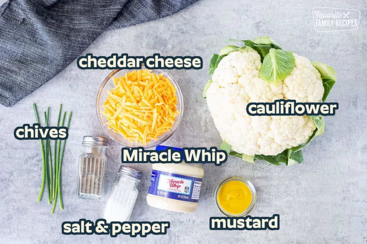 Ingredients to make Cheesy Cauliflower side dish including head of cauliflower, mustard, miracle whip, cheddar cheese, salt, pepper and chives.