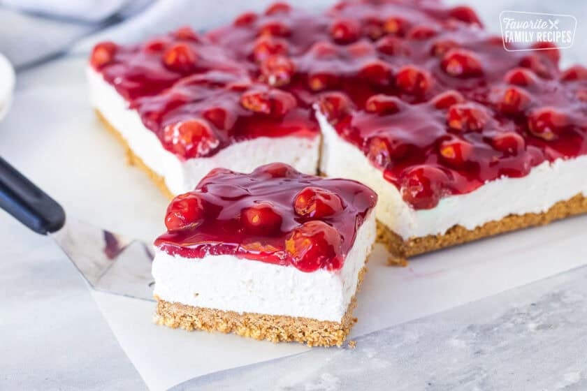 Slice of cherry delight recipe with a graham cracker crust, cream cheese filling and cherry topping.