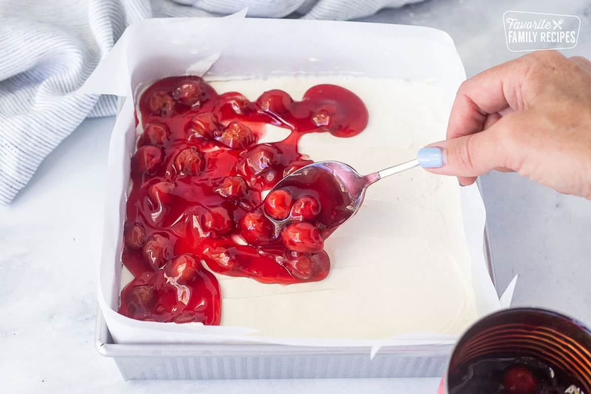 Spooning cherry pie filling onto cream cheese filling.