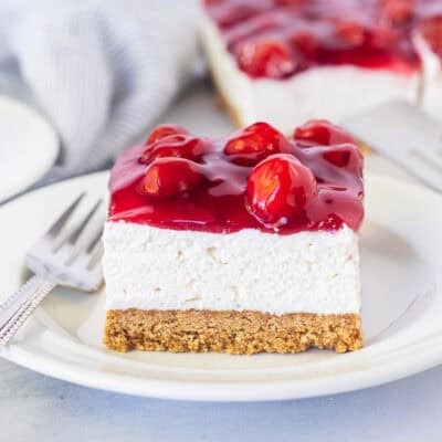 Plate with a slice of cherry delight recipe with a graham cracker crust, cream cheese filling and cherry topping.
