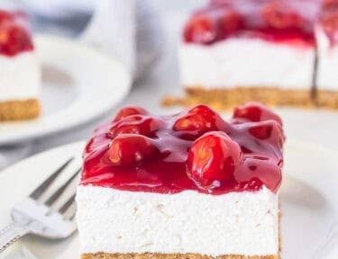 Slice of cherry delight recipe with a graham cracker crust, cream cheese filling and cherry topping on a plate.