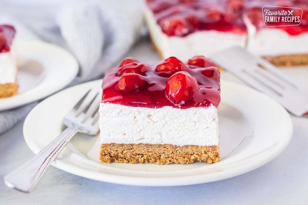 Plate with a slice of cherry delight recipe with a graham cracker crust, cream cheese filling and cherry topping.
