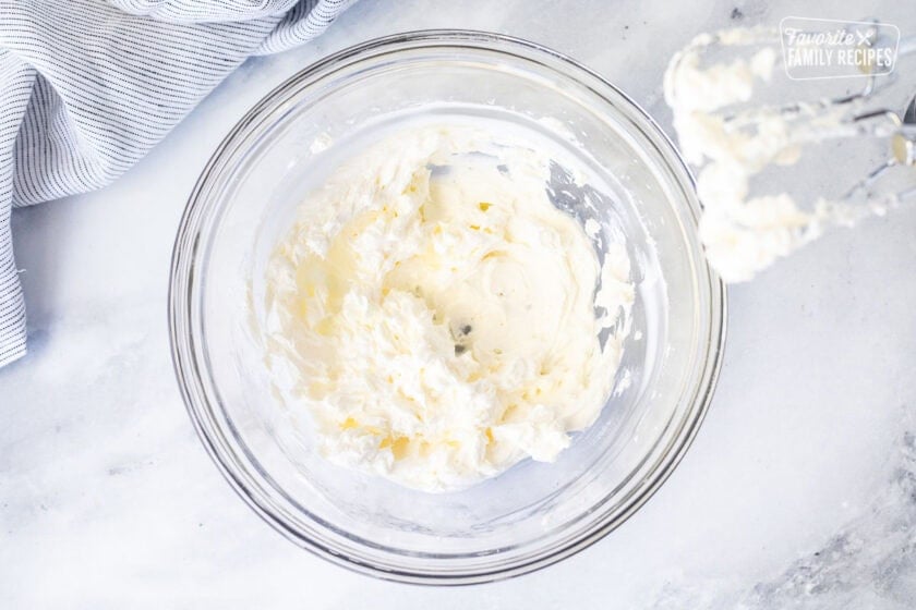 Whipped cream cheese in a glass bowl with beaters.