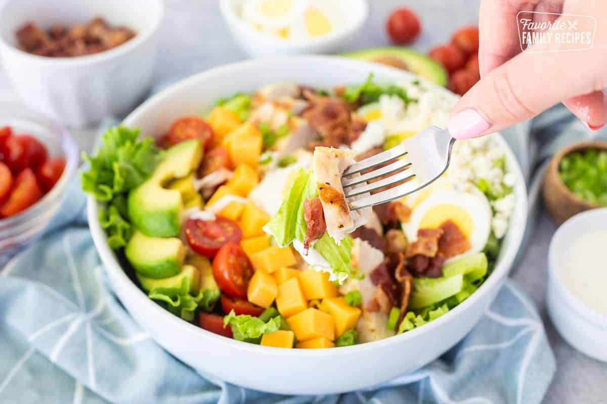 Bite of Cobb salad with chicken, lettuce and bacon on the fork.