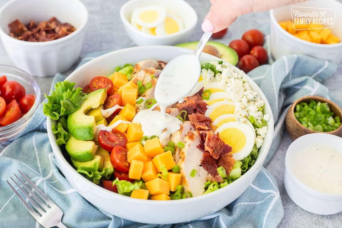Spooning Ranch dressing on top of Cobb salad in a bowl.