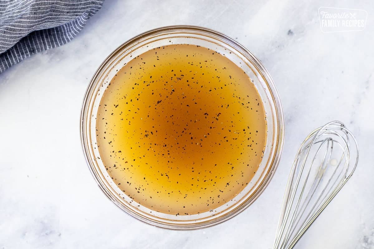 Glass bowl with dressing mixed and whisk on the side.