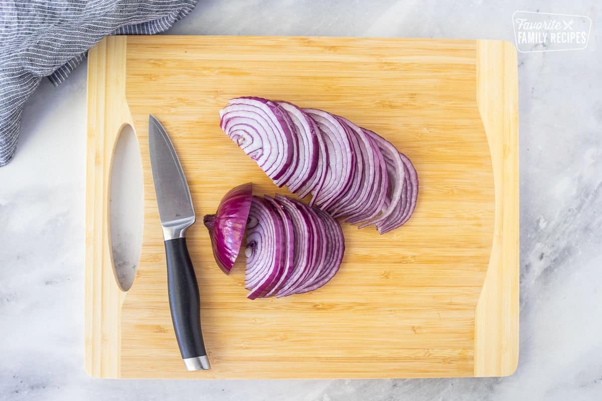 Sliced red onion on a cutting board with a knife.