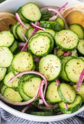 Tongs picking up cucumber vinegar salad with sliced cucumbers and red onion.