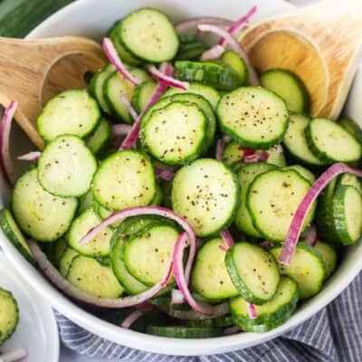Tongs picking up cucumber vinegar salad with sliced cucumbers and red onion.