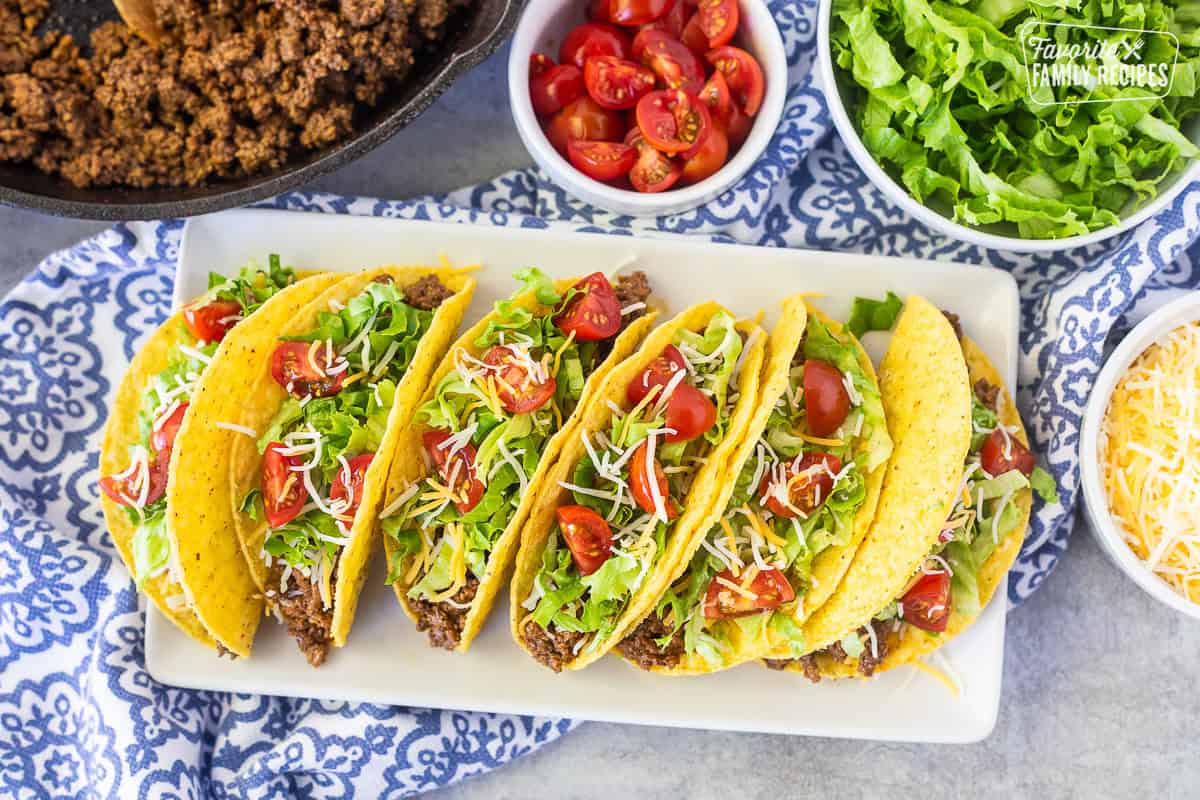 Platter of ground beef tacos with a crunchy shell, seasoned ground beef, lettuce, cheese and tomatoes.