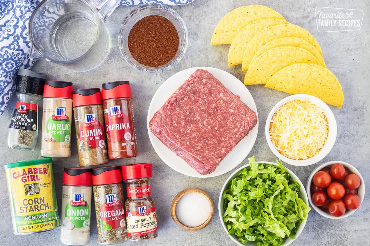 Ingredients to make ground beef tacos including ground beef, taco shells, cheese, tomatoes, lettuce, salt, chili powder, water, black pepper, garlic powder, cumin, paprika, corn starch, onion powder, oregano, and crushed red pepper.