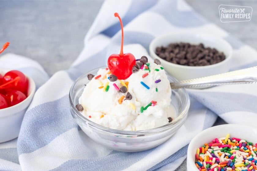 Small dish with homemade ice cream scoops from bag and topped with sprinkles, chocolate chips and a cherry.
