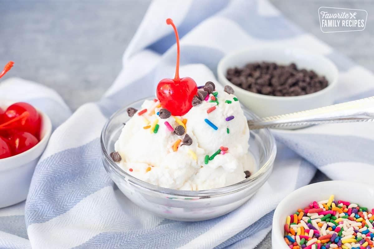 Small dish with homemade ice cream scoops from bag and topped with sprinkles, chocolate chips and a cherry.