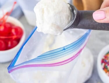 Scoop of homemade ice cream from a bag. Cones, sprinkles, cherries and chocolate chips on the side.
