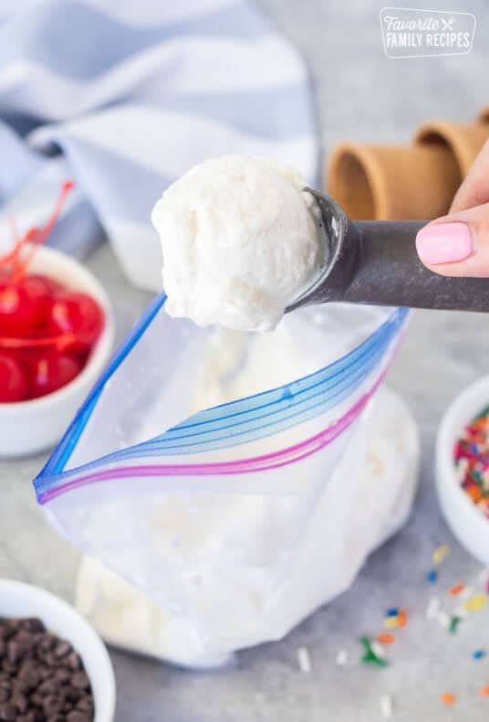 Scoop of homemade ice cream from a bag. Cones, sprinkles, cherries and chocolate chips on the side.