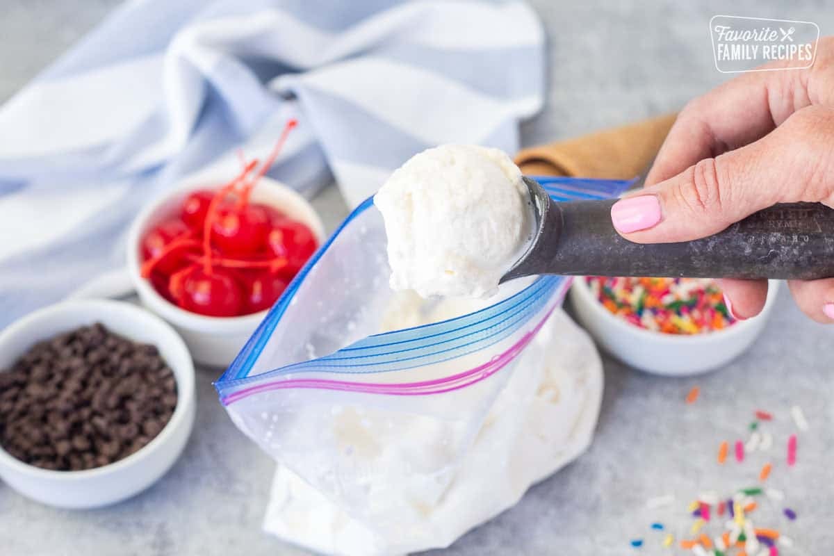 Scoop of homemade ice cream from a bag. Cones, sprinkles, cherries and chocolate chips on the side.