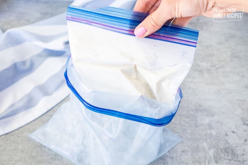 Pulling smaller ice cream bag out of larger bag of ice and salt.