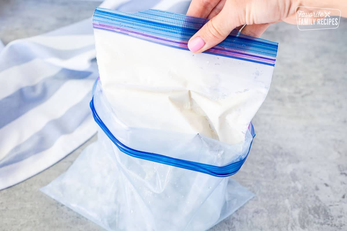 Pulling smaller ice cream bag out of larger bag of ice and salt.