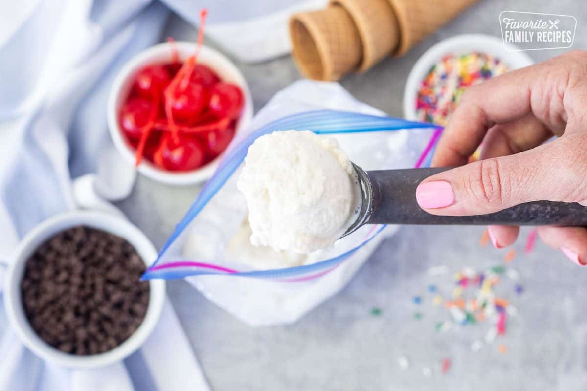 Scoop of homemade ice cream from a bag. Cones, sprinkles, cherries and chocolate chips on the side.
