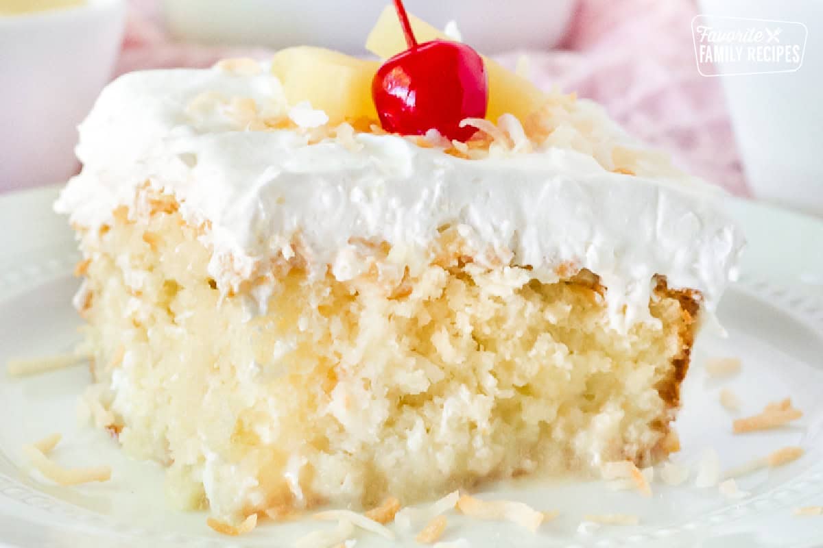 Close up of a Pina Colada Cake slice garnished with toasted coconut, pineapple and a cherry.