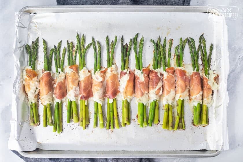 Sheet pan with baked prosciutto wrapped asparagus bundles.