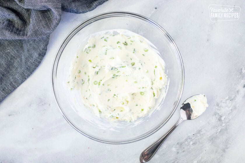 Glass mixing bowl with cream cheese, green onion and garlic mixture. Spoon on the side.