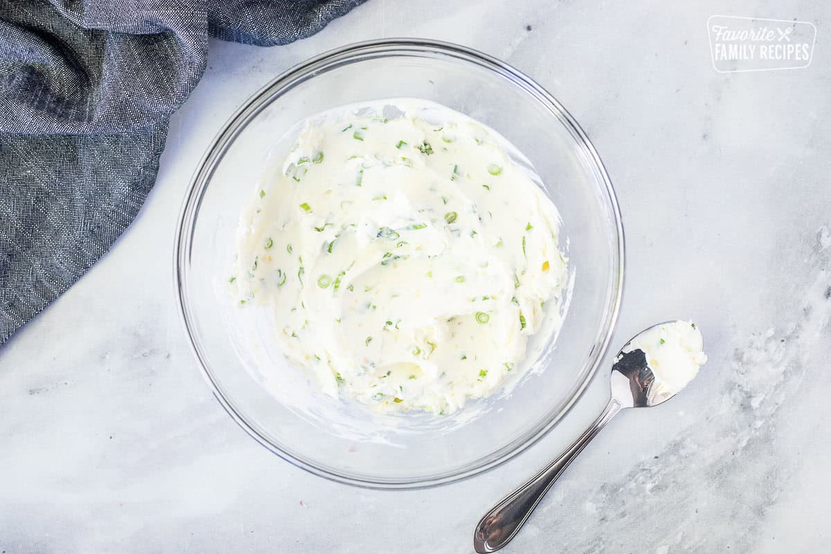 Glass mixing bowl with cream cheese, green onion and garlic mixture. Spoon on the side.