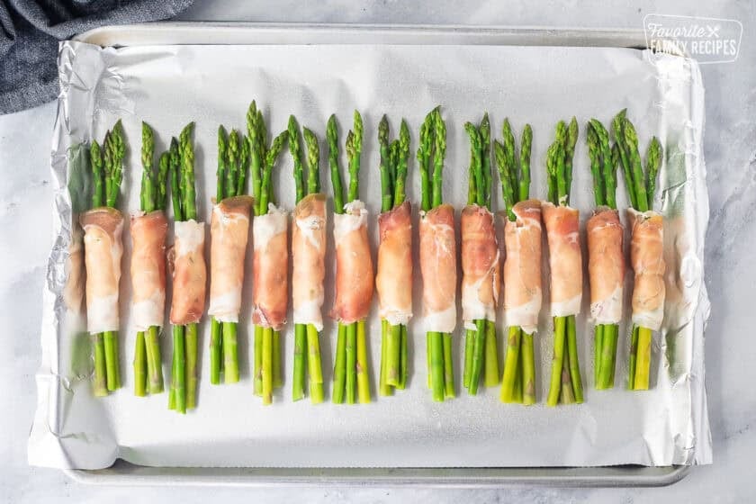 Sheet pan with uncooked asparagus wrapped with prosciutto bunches.