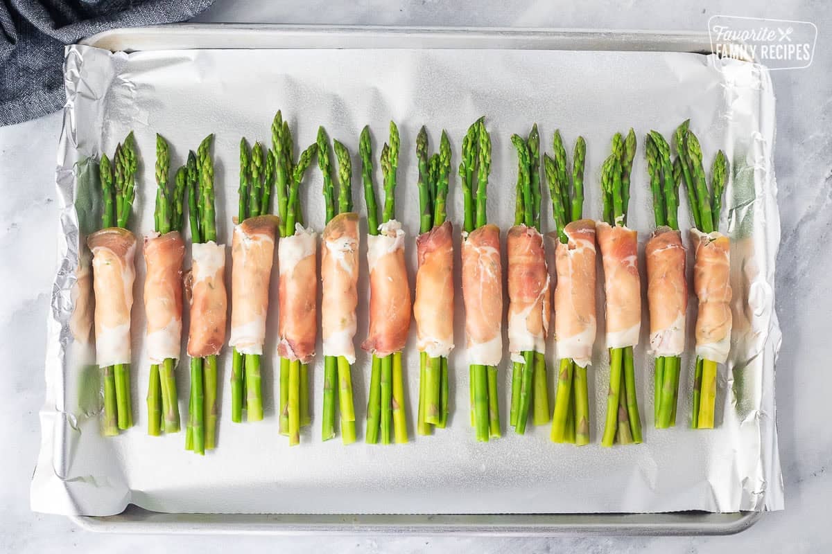 Sheet pan with uncooked asparagus wrapped with prosciutto bunches.