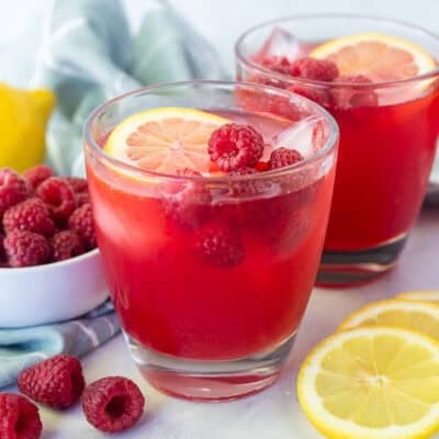 Glasses of raspberry cordial topped with fresh lemon slice and fresh raspberries.