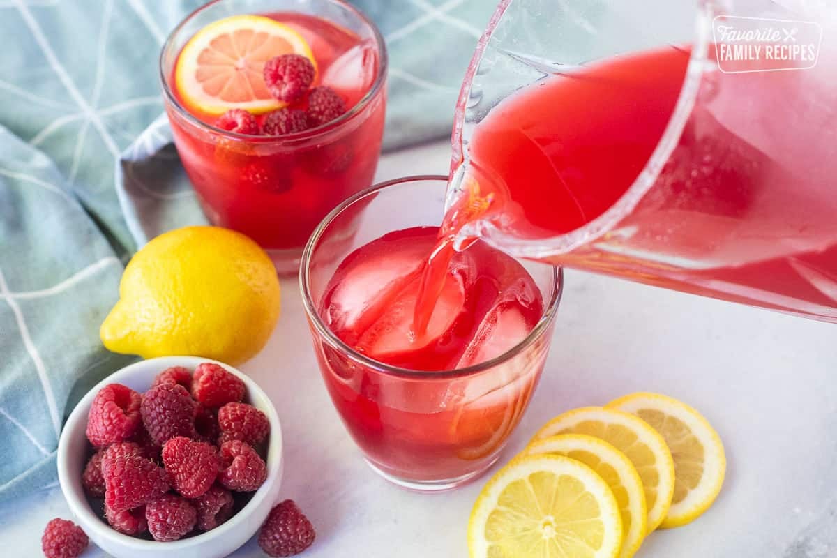 Pouring raspberry cordial into a glass with ice.